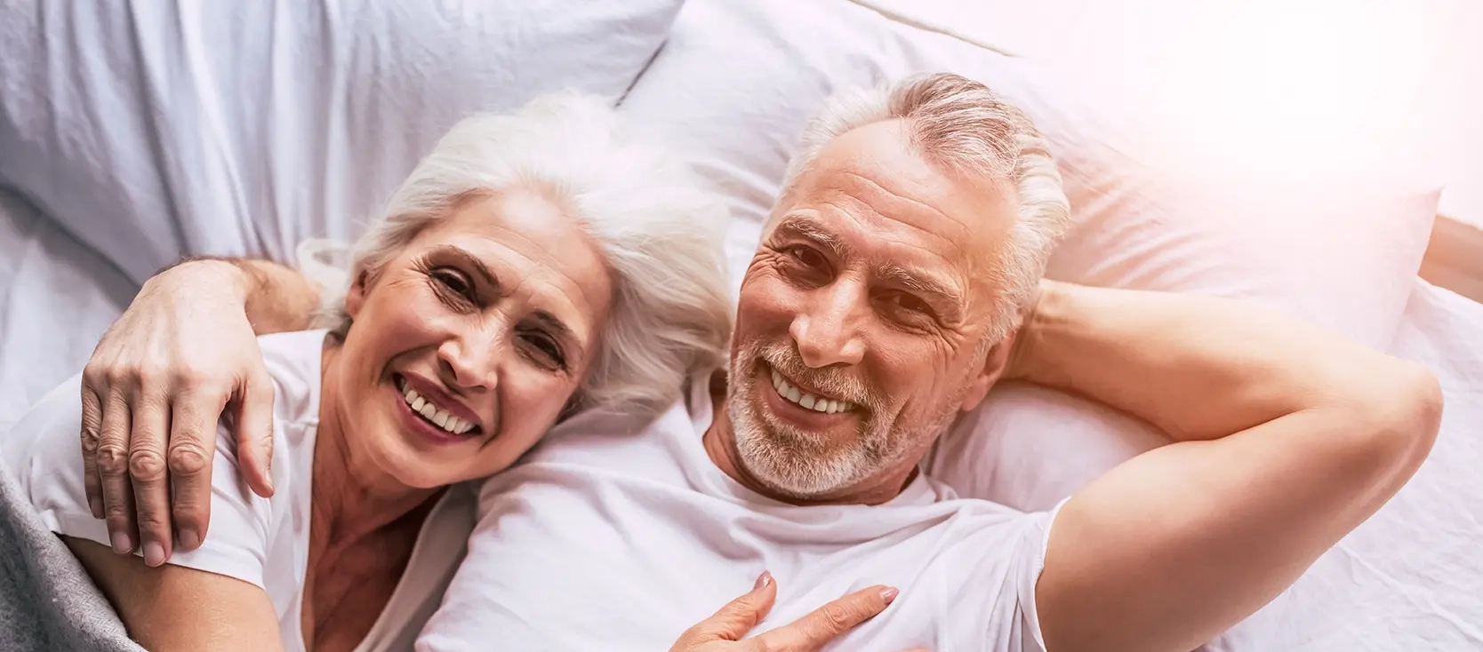Ein älteres Ehepaar liegt zusammen im Bett und lacht.